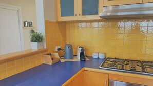 A kitchen with wooden cabinets, a gas stove, a kettle, and a small plant on the counter.