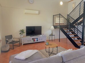 A living room with a sofa, a television, a bookshelf, a plant, a lamp, and a staircase.