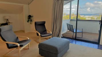 A room with two armchairs, a sofa, a small table, and a view of a balcony with chairs.