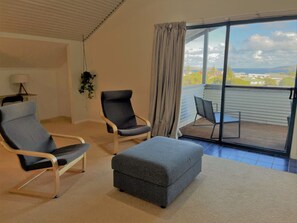A room with two armchairs, a sofa, a small table, and a view of a balcony with chairs.