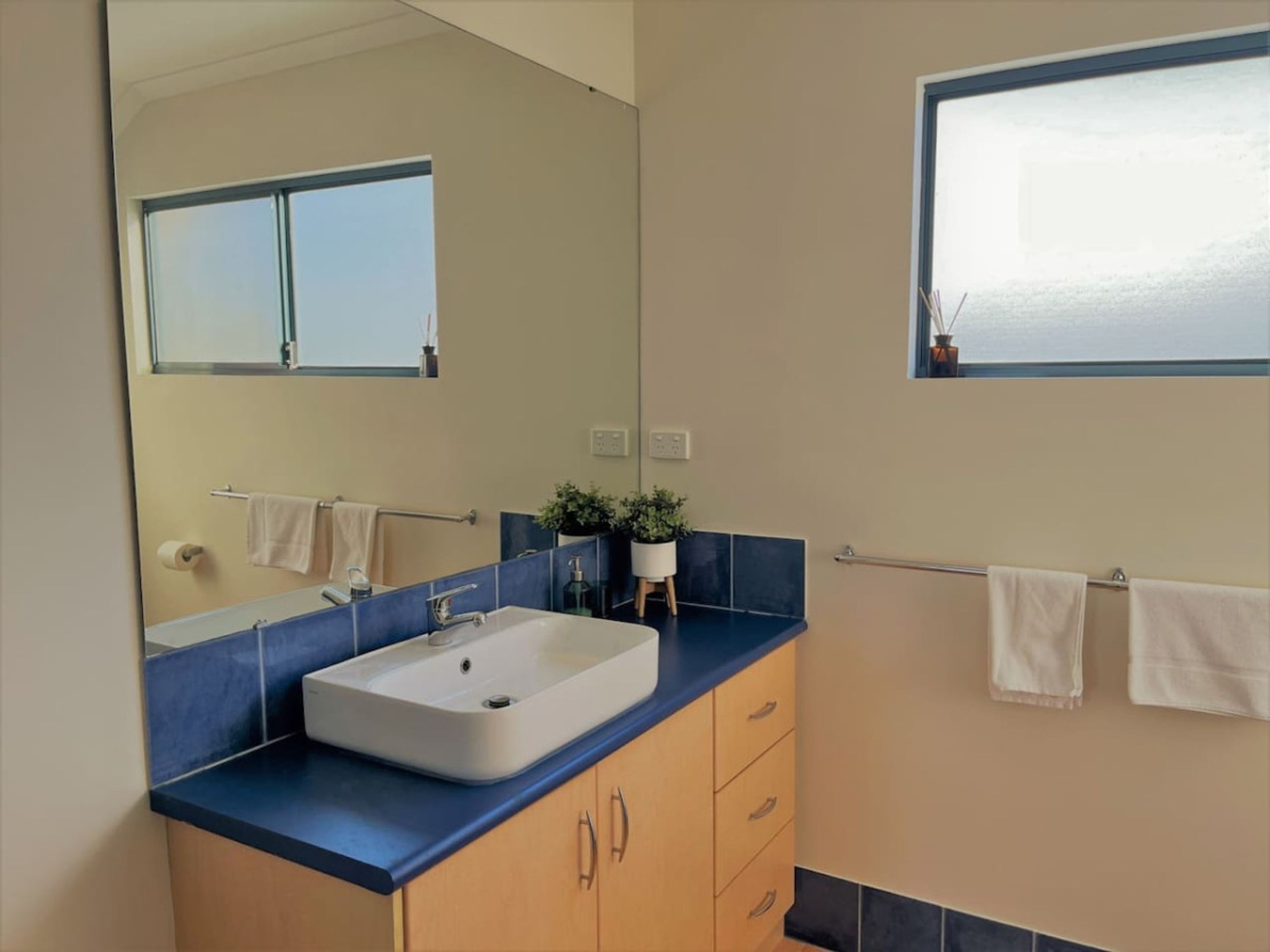 Un baño con un espejo grande, un lavabo, una ventana y toallas en un perchero.