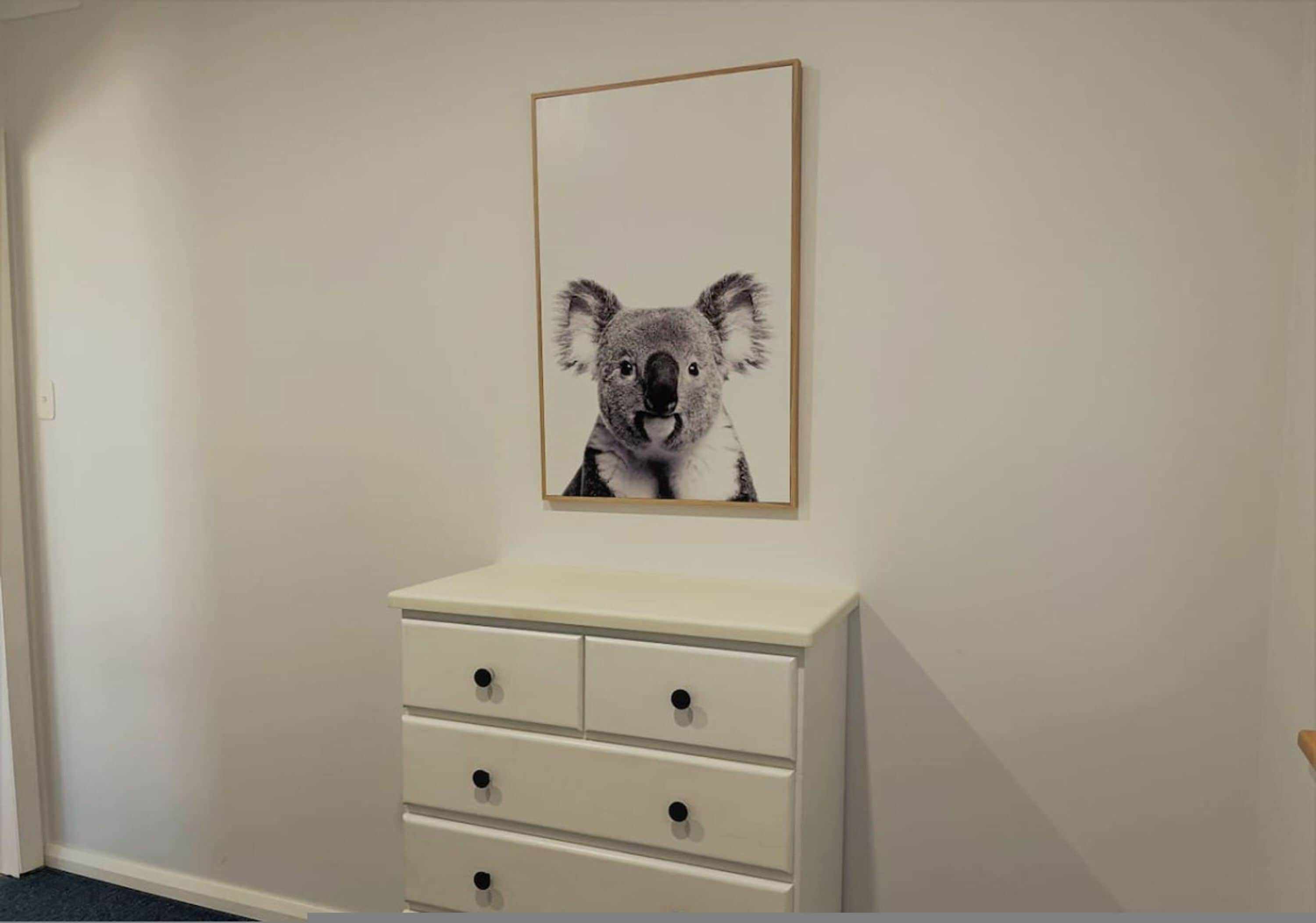 A room with a white dresser and a framed picture of a koala on the wall.