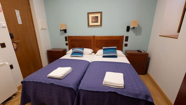A double bed with a wooden headboard, two bedside tables, a wall-mounted lamp, and a framed picture above the bed. - La Juderia Segovia Lodging (Segovia)