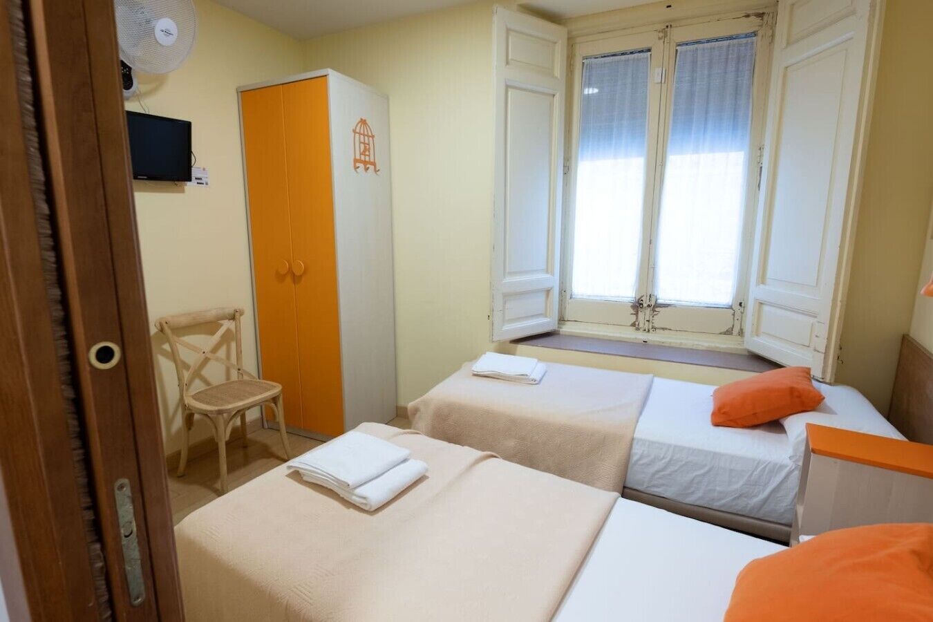 Une chambre avec deux lits, une chaise, une armoire et une fenêtre avec des rideaux.