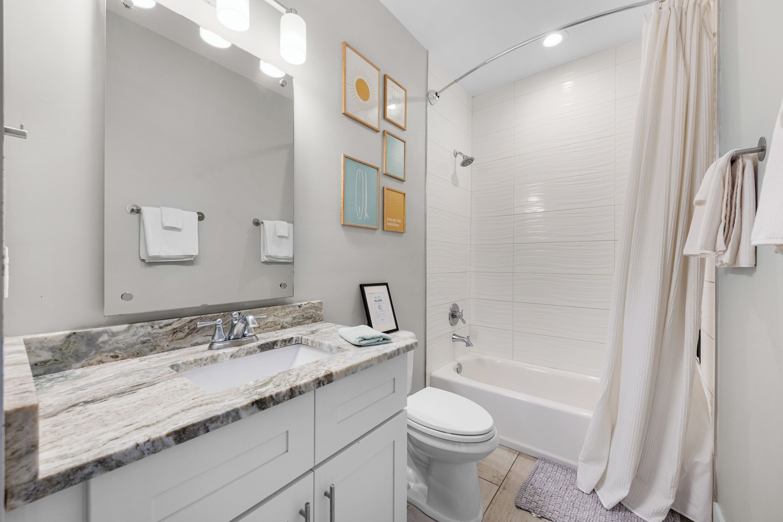 Un baño moderno con encimera de mármol, inodoro blanco, bañera y cuadros enmarcados en la pared.