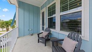 A covered porch with two Adirondack chairs, a small table, and a window with blinds. - Sunny 3BR Getaway | Good Morning Rentals (Jacksonville Beach)