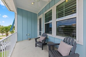 A covered porch with two Adirondack chairs, a small table, and a window with blinds. - Sunny 3BR Getaway | Good Morning Rentals (Jacksonville Beach)