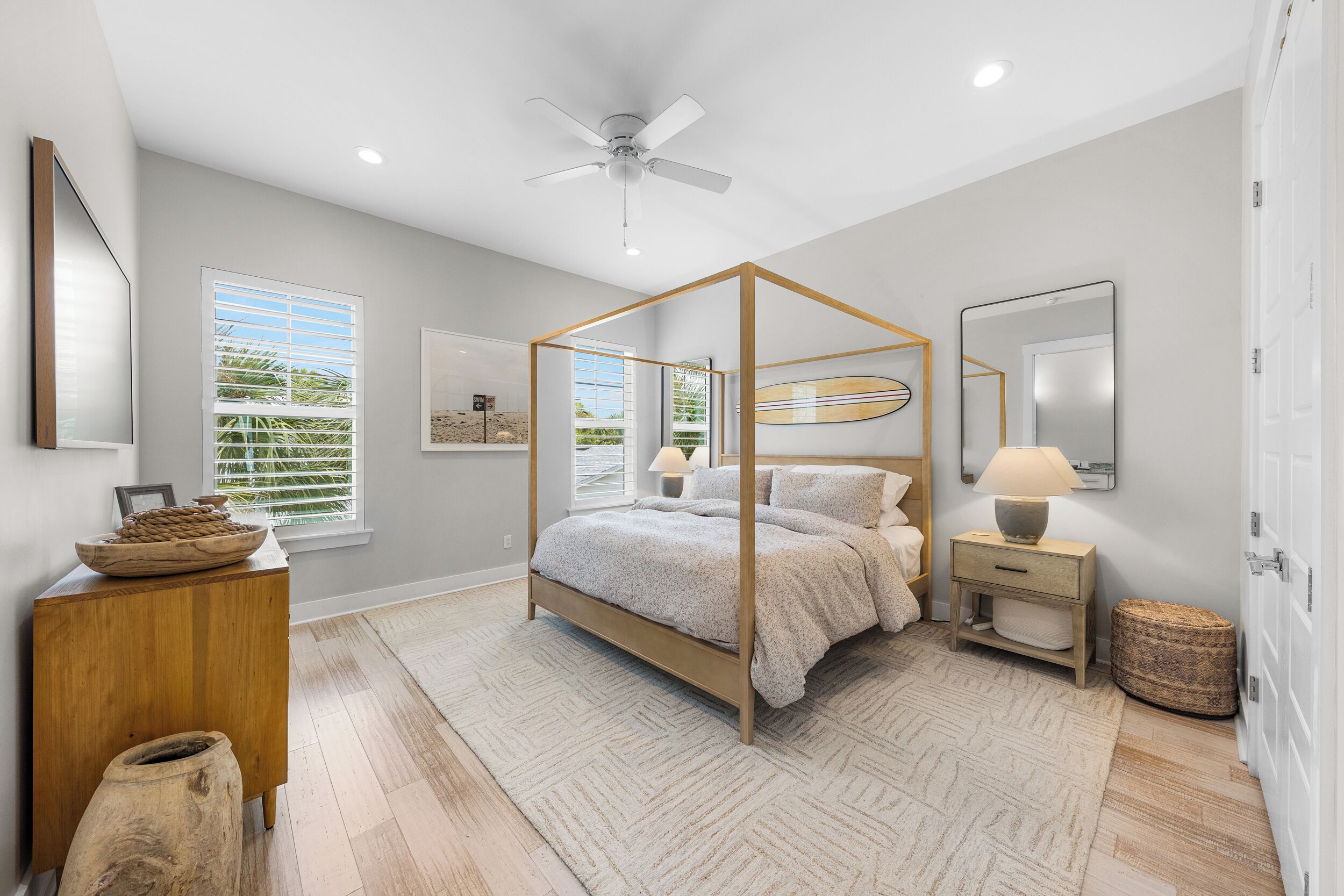A bedroom with a four-poster bed, a ceiling fan, and a large window with blinds.