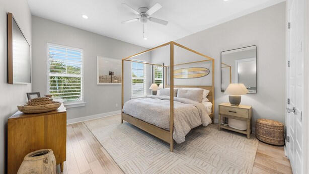 A bedroom with a four-poster bed, a ceiling fan, and a large window with blinds. - Sunny 3BR Getaway | Good Morning Rentals (Jacksonville Beach)