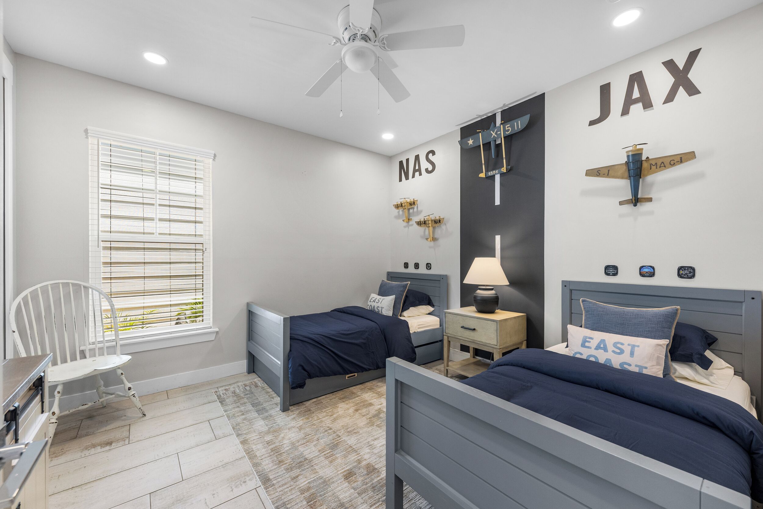 A bedroom with two beds, a window with blinds, a ceiling fan, and a wall with a large 'JAX' sign.