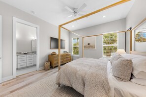 Ein Schlafzimmer mit Baldachinbett, Fernseher, Kommode und Blick auf Palmen durch das Fenster.