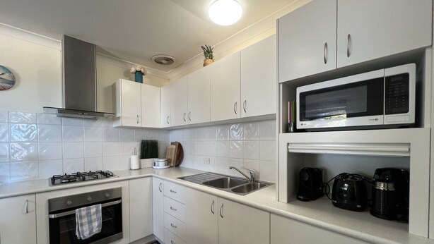 A modern kitchen with white cabinetry, a gas stove, a microwave, and a coffee maker.