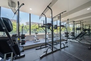 Uma academia com diversos equipamentos de exercício, grandes janelas e vista para o exterior.