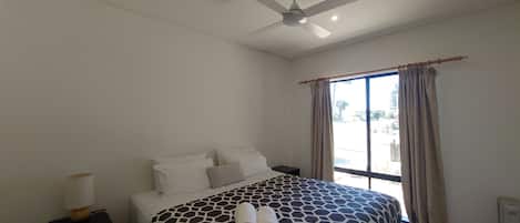 A hotel room with a bed, a ceiling fan, a nightstand, and a window with curtains.