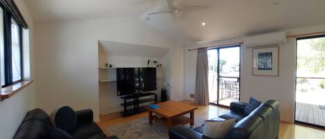 A living room with a flat-screen TV, a wooden coffee table, two sofas, and a ceiling fan.