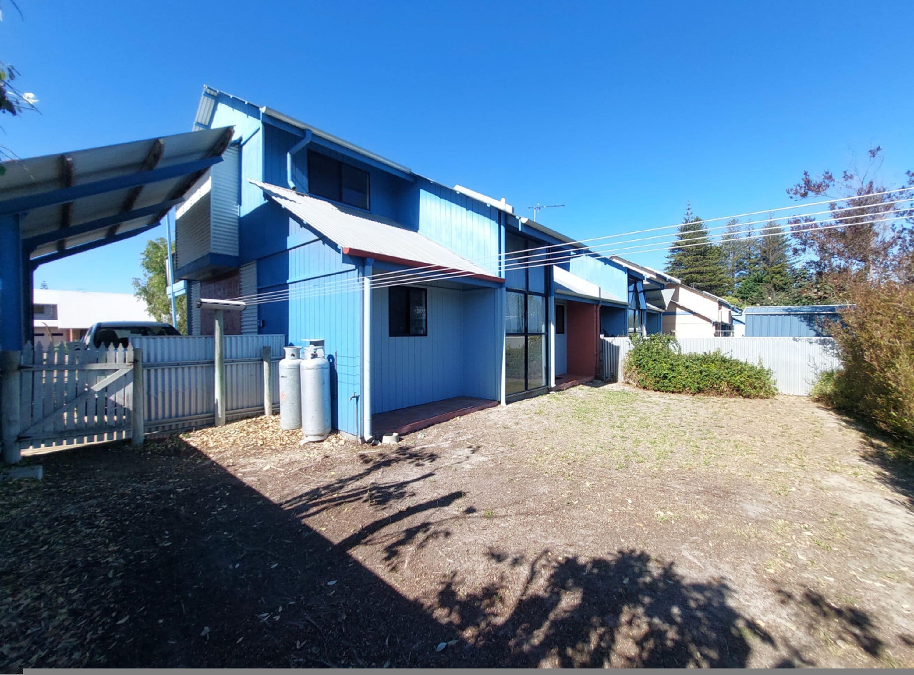A blue building with a covered porch, a fenced yard, and two propane tanks.