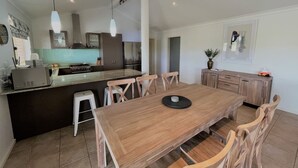 A modern kitchen with a central island, wooden dining table, and chairs. - The Willow in West Beach (Esperance)