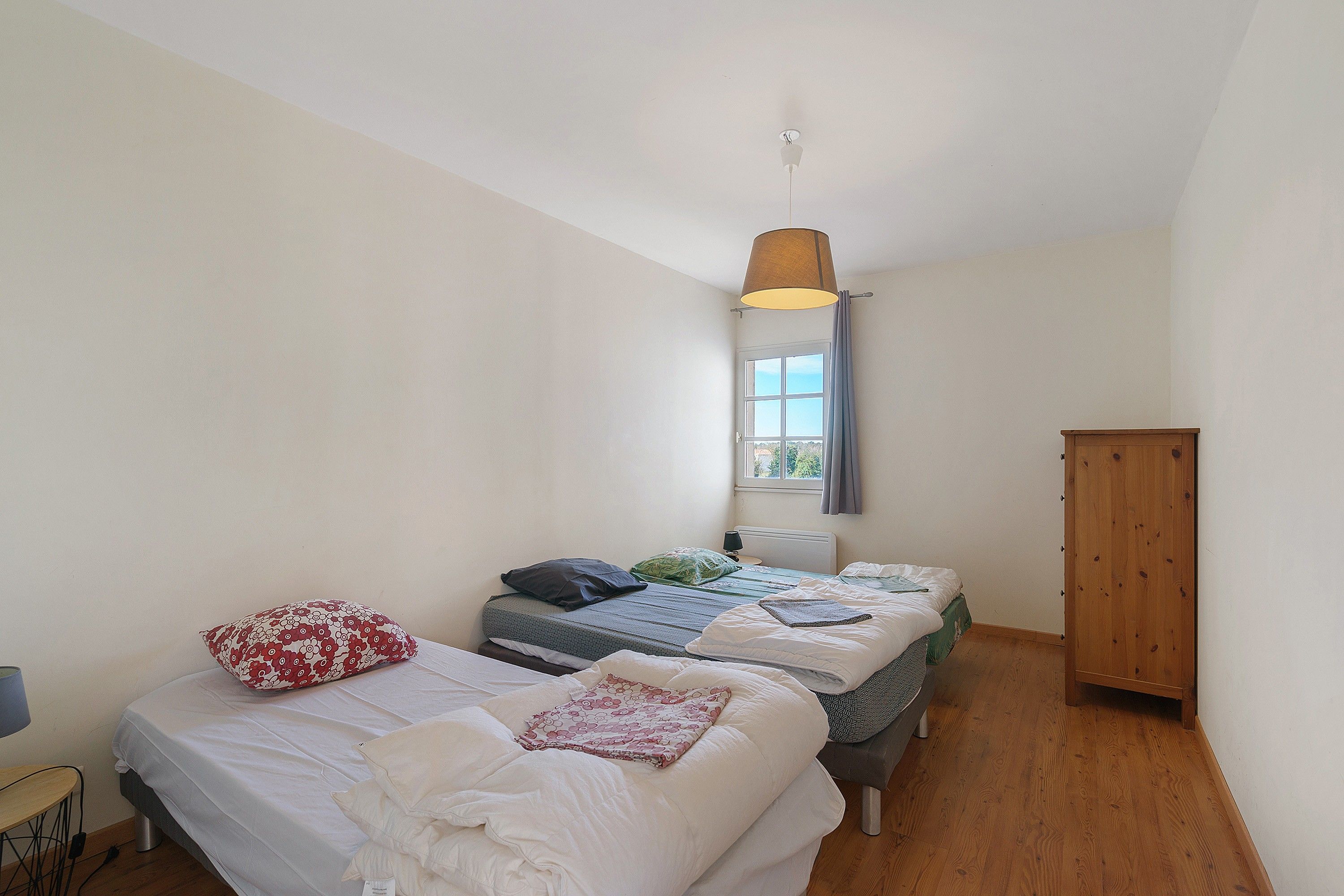 Un dormitorio con dos camas individuales, un armario de madera, una ventana con cortinas y una lámpara colgante.