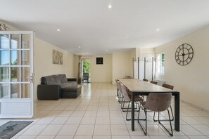 A spacious dining area with a long table and chairs, a sofa, and a wall clock.