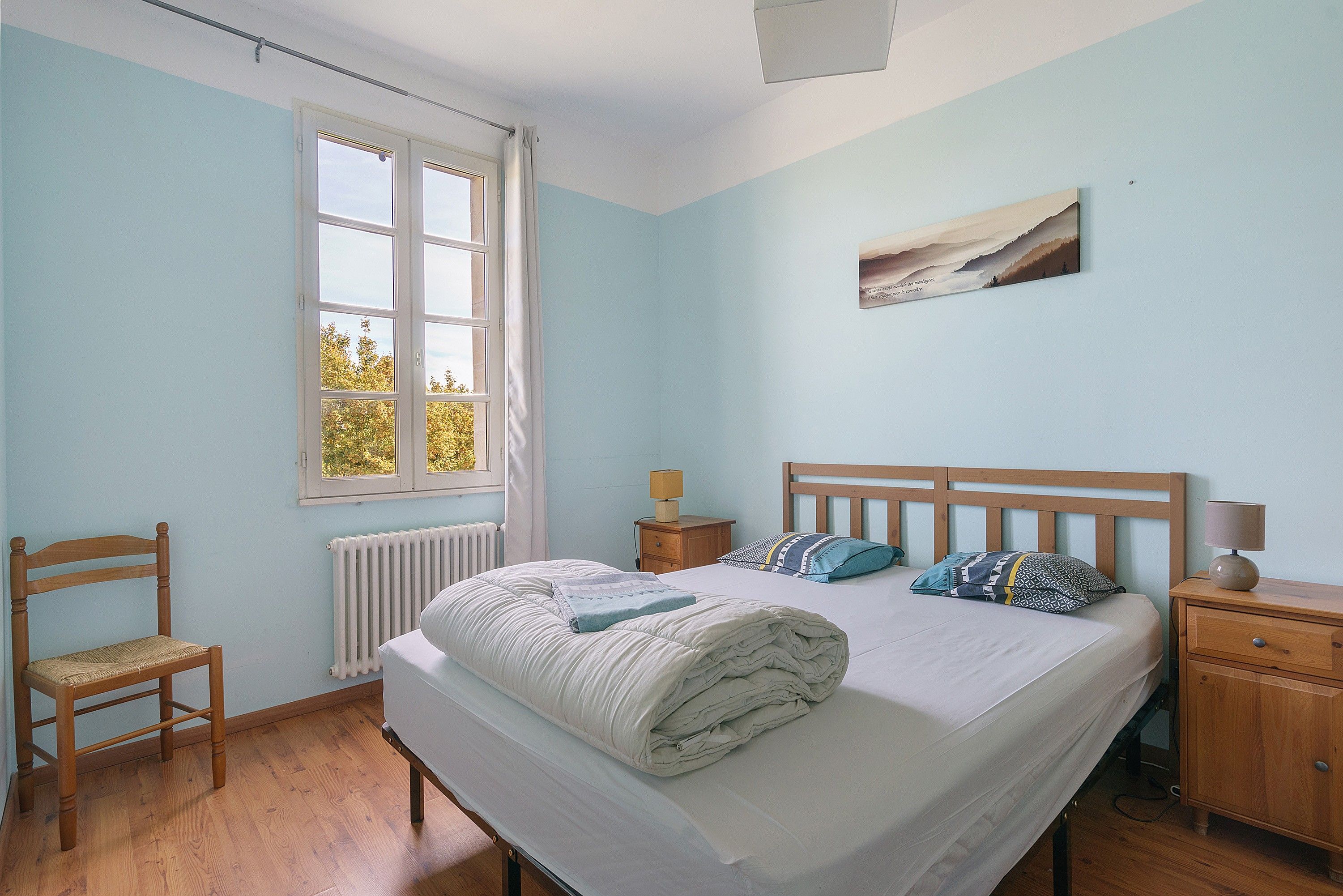 A bedroom with a bed, a chair, a nightstand, a lamp, and a window.
