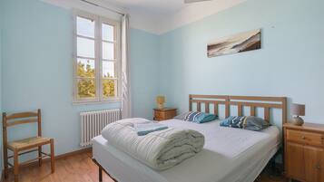 A bedroom with a bed, a chair, a nightstand, a lamp, and a window.