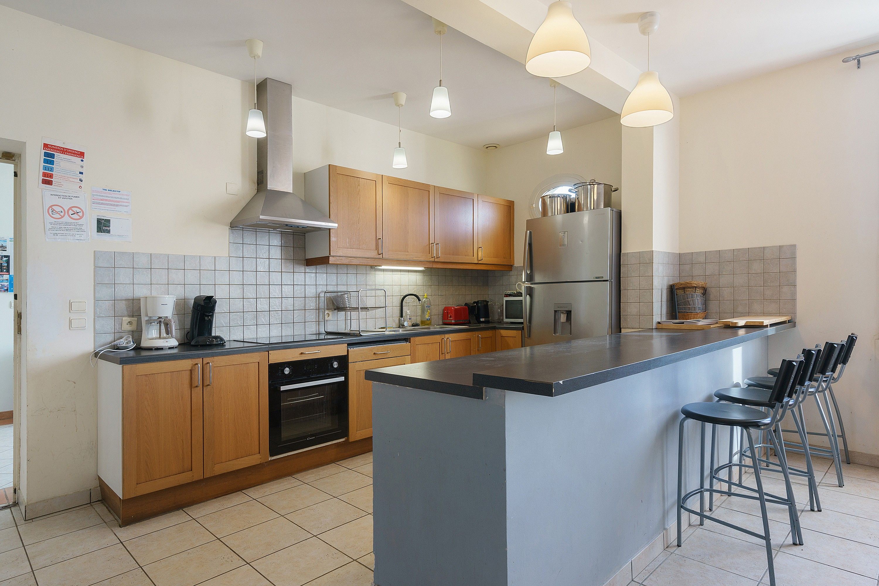 A modern kitchen with wooden cabinets, a stainless steel refrigerator, and a bar area with stools.
