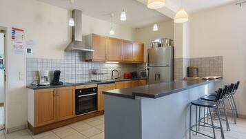 A modern kitchen with wooden cabinets, a stainless steel refrigerator, and a bar area with stools.