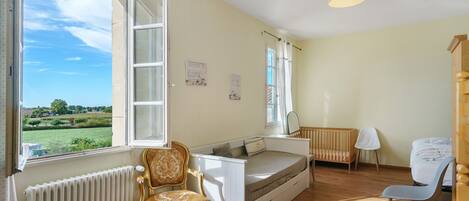 A room with a bed, a chair, a desk, a radiator, and a window with an open shutter.