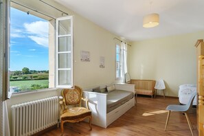 Una habitación con cama, una silla, un escritorio, un radiador y una ventana con persiana abierta.