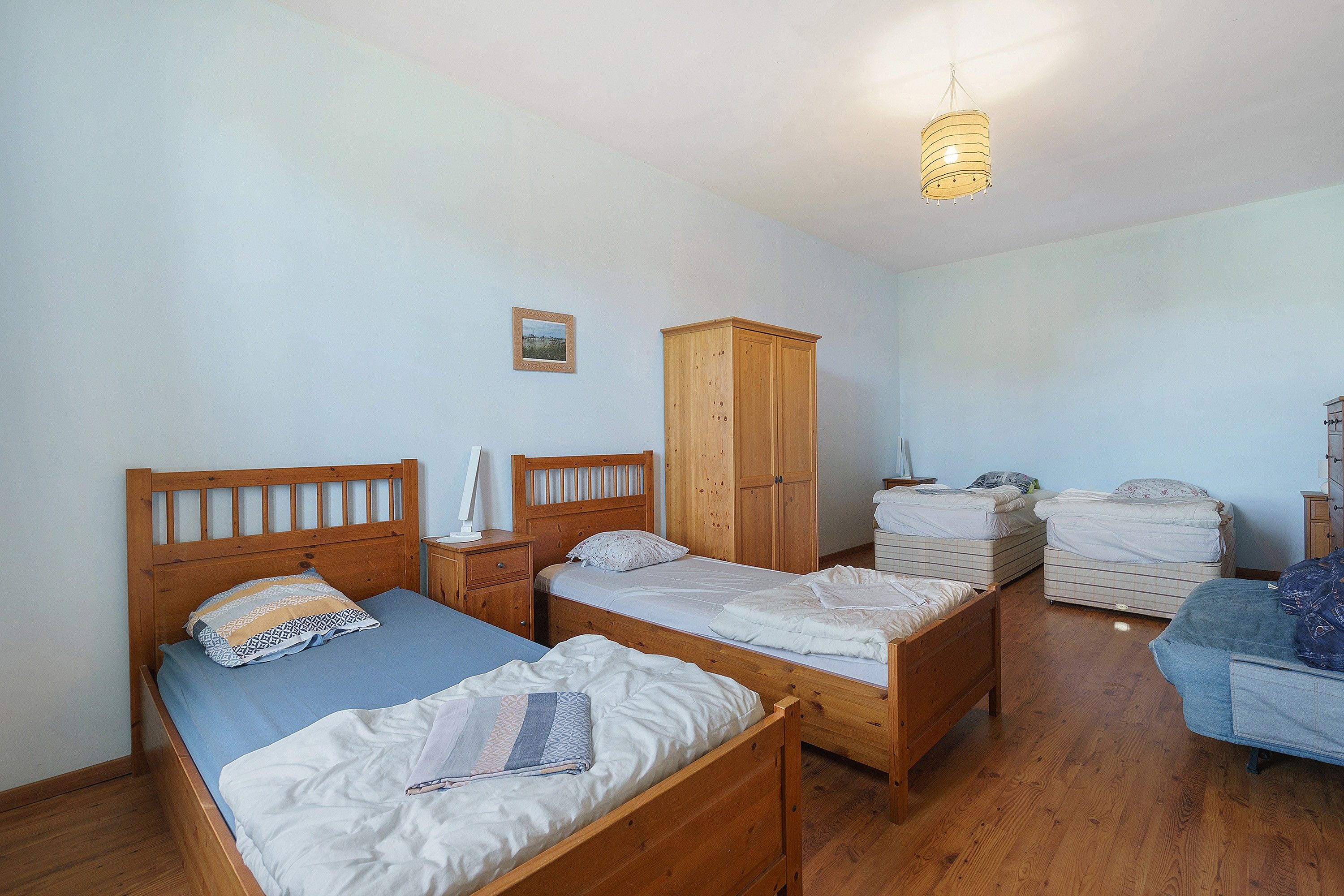 A bedroom with two wooden beds, a wardrobe, and a hanging light fixture.