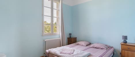 A bedroom with a bed, a nightstand, a dresser, a window with curtains, and a radiator.