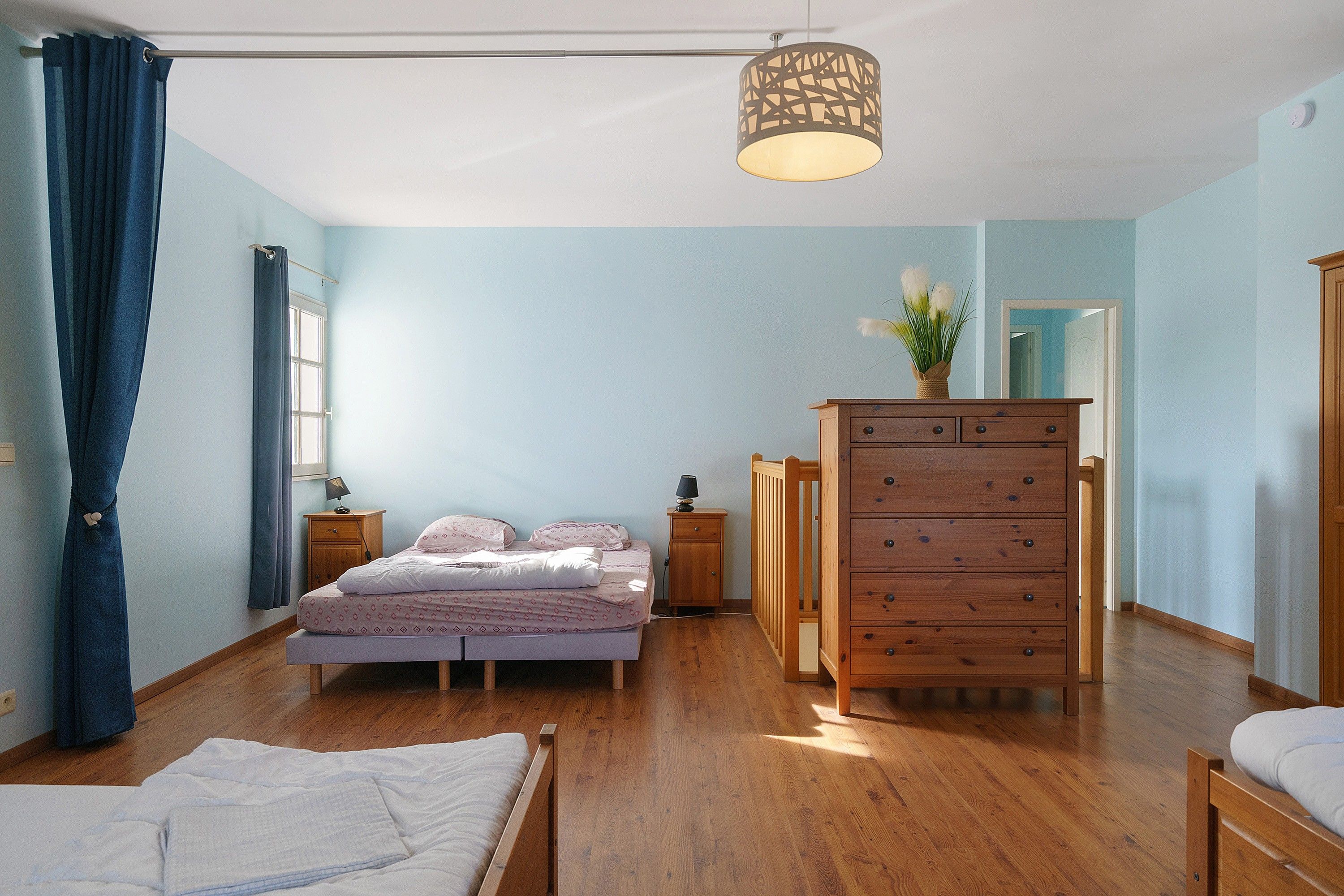 A bedroom with a bed, dresser, nightstands, and a hanging light fixture.