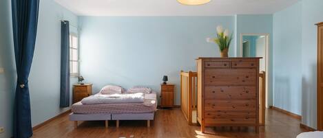 A bedroom with a bed, dresser, nightstands, and a hanging light fixture.