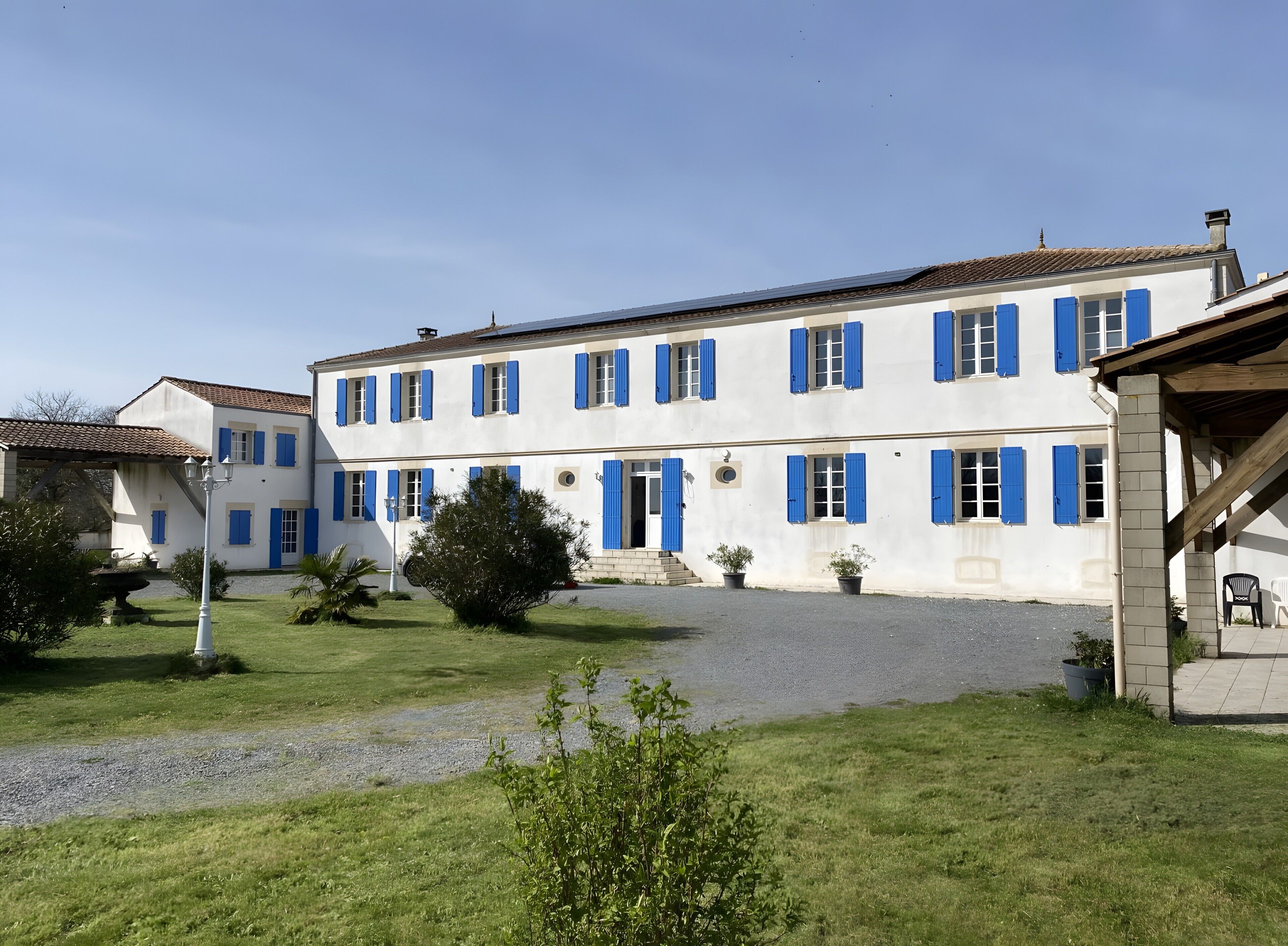 Un bâtiment blanc avec des volets bleus et une allée gravillonnée.