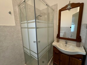 A bathroom with a glass shower enclosure, a wooden vanity with a sink, and a mirror with a wooden frame. - Nicola House (Catania)