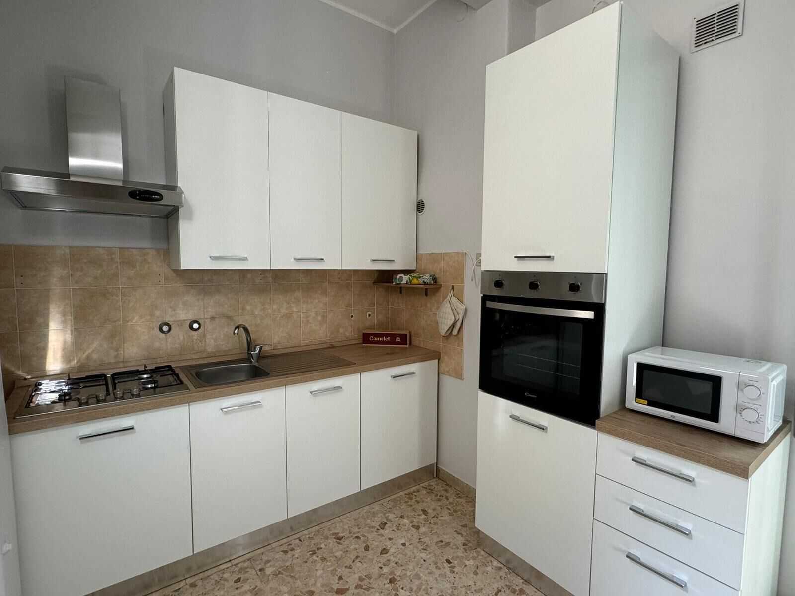 Una cocina con gabinetes blancos, estufa a gas, microondas y horno integrado.