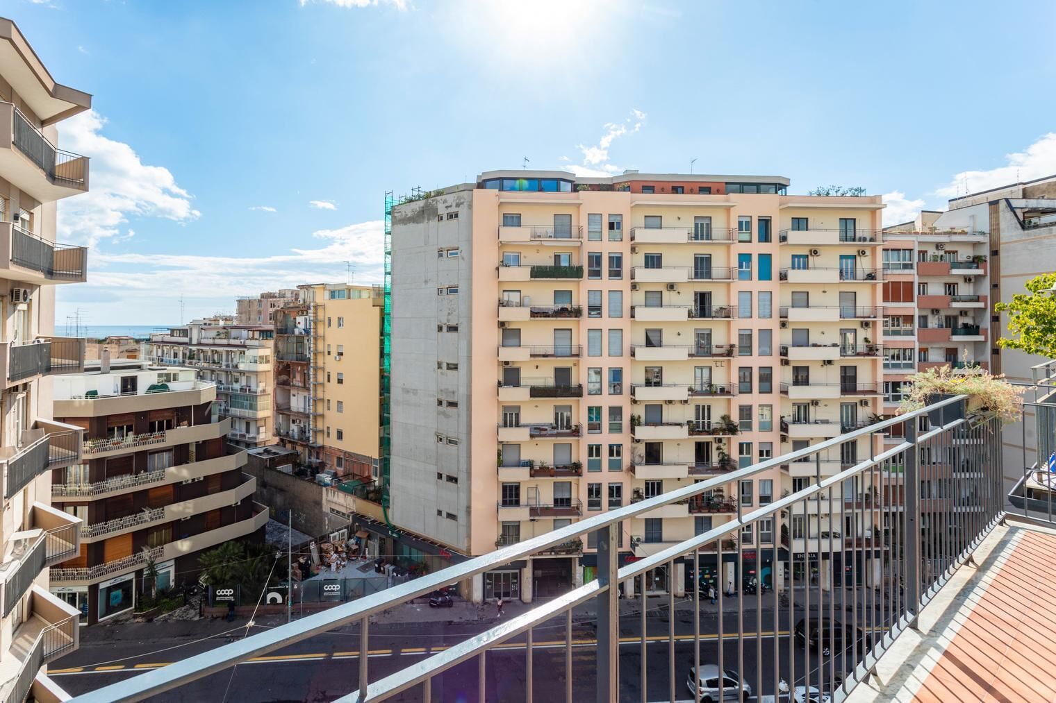 A multi-story residential building with balconies, a pedestrian street below, and a clear sky.