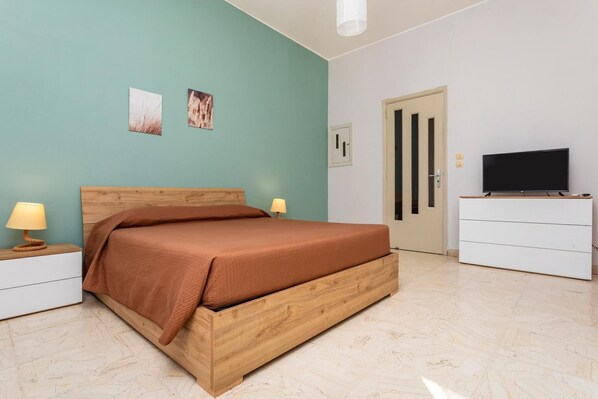 A bedroom with a wooden bed, bedside tables, a television, and a door. - Nicola House (Catania)