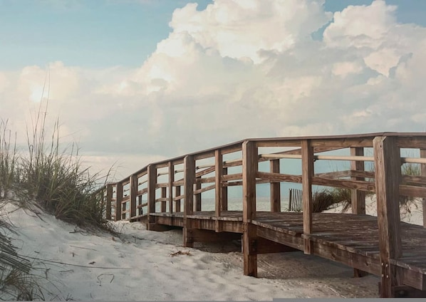 A wooden boardwalk leading to a beach with sand dunes and sparse vegetation.