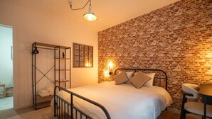 A bedroom with a brick wall, a bed with a metal frame, a bedside table, and a chair. - Le Coin du Diable (Bruxelles)