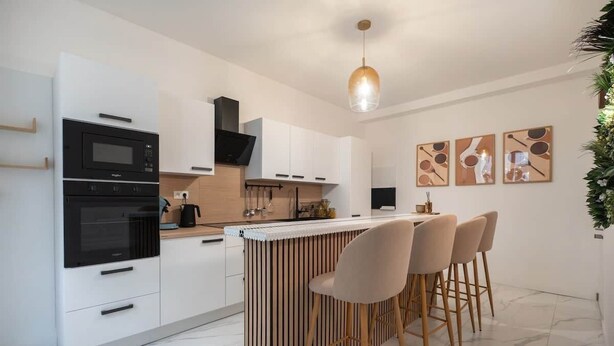A modern kitchen with a central island, bar stools, and a hanging light fixture. - Le Coin du Diable (Bruxelles)