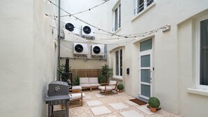 A courtyard with a grill, seating area, and string lights.