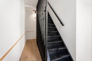 Eine Treppe mit schwarzen Stufen und einem Holnänder, die zu einer Zwischenebene mit einer Leuchte führen.