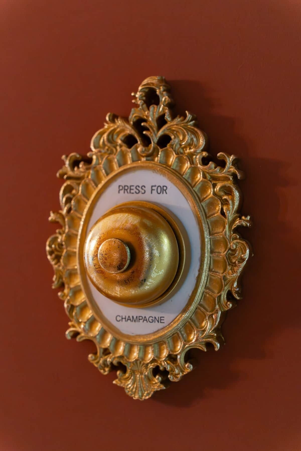 Um botão decorativo com o texto 'PRESS FOR CHAMPAGNE' em fundo vermelho.