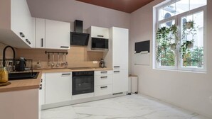 A modern kitchen with white cabinets, a wooden countertop, and a large window with plants. - Chez Thérèse (Bruxelles)