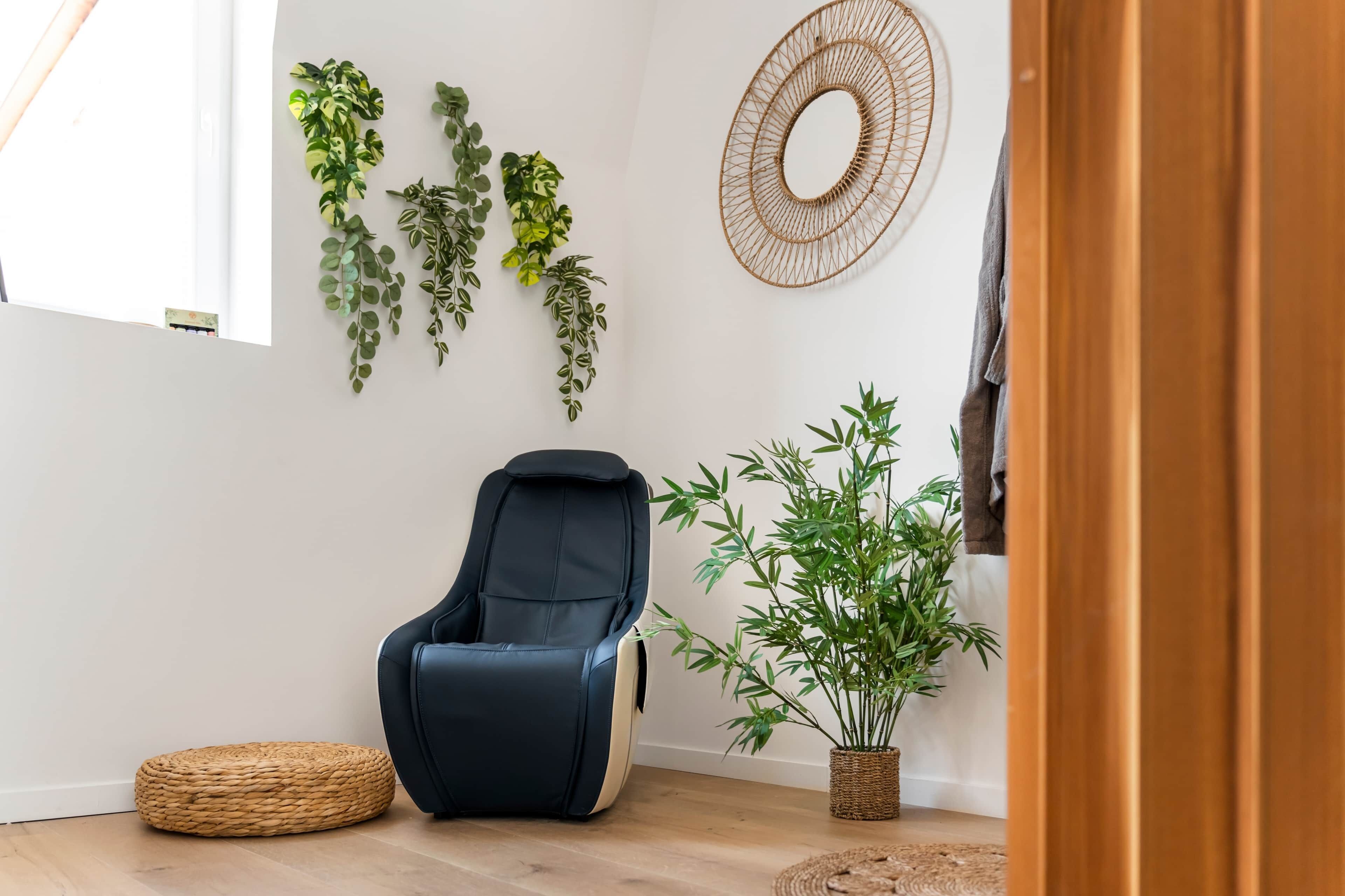 Een kamer met een zwarte massagestoel, een geweven zitkussen en een bamboeplant in een rieten pot.