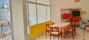 Een kamer met een eettafel, stoelen, een bank, een televisie en een raam met gordijnen.
