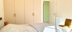 A bedroom with a bed, a wardrobe, a radiator, and a chair. - Les Balcons Du Levant Beirut by Hansa (Beirut)