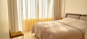 Un dormitorio con cama, una silla y una ventana con cortinas.