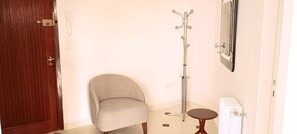 Een kamer met een houten deur, een grijze fauteuil, een radiator en een klein, rond tafeltje.